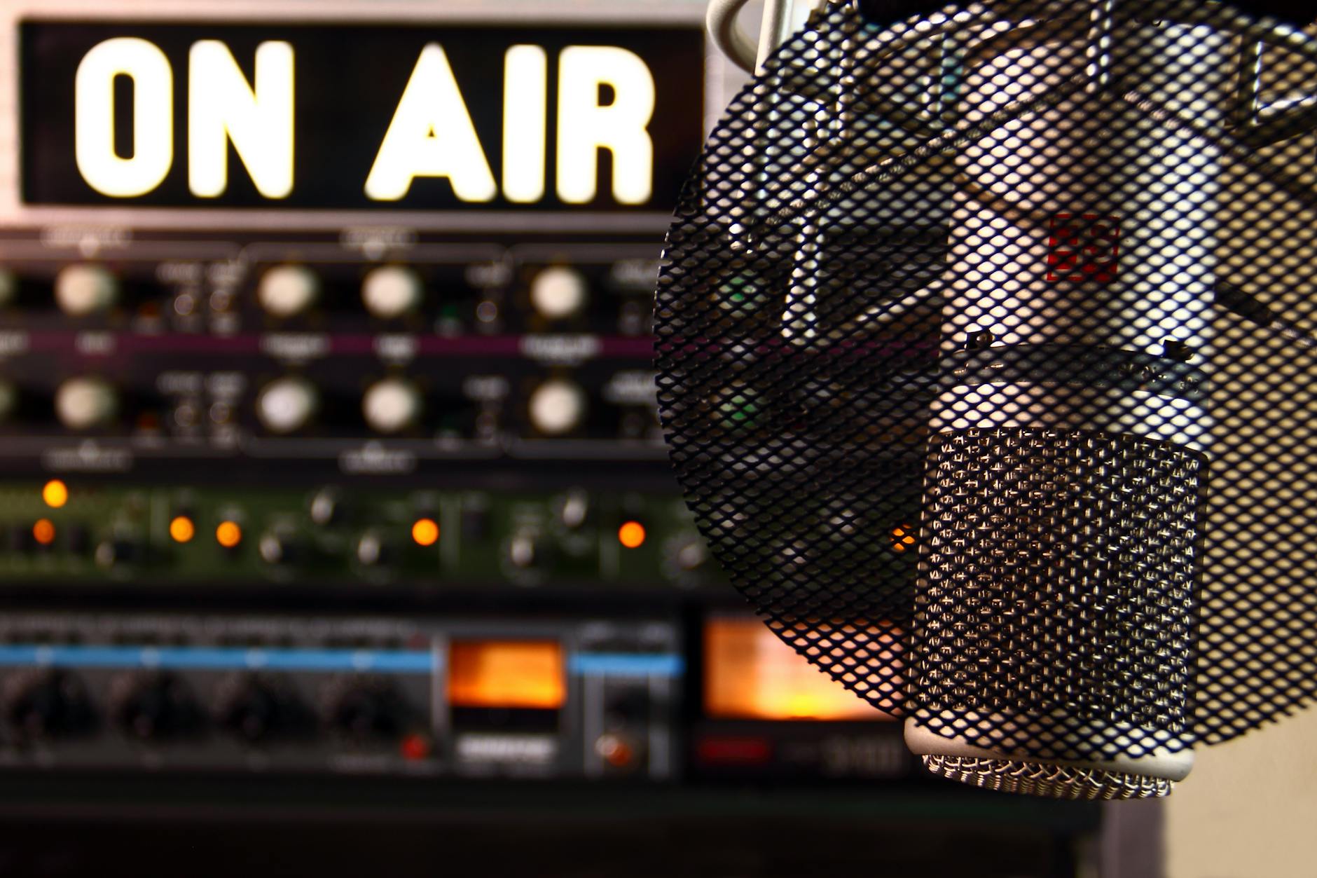on air lit sign above radio machines. in the foreground is a microphone with a protective screen