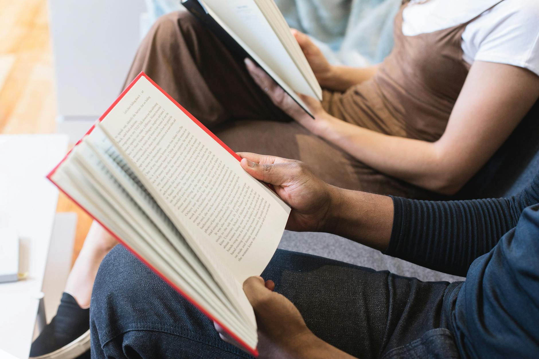 view of two people reading showing them sitting with only a view of their hands, laps and the books they are holding.