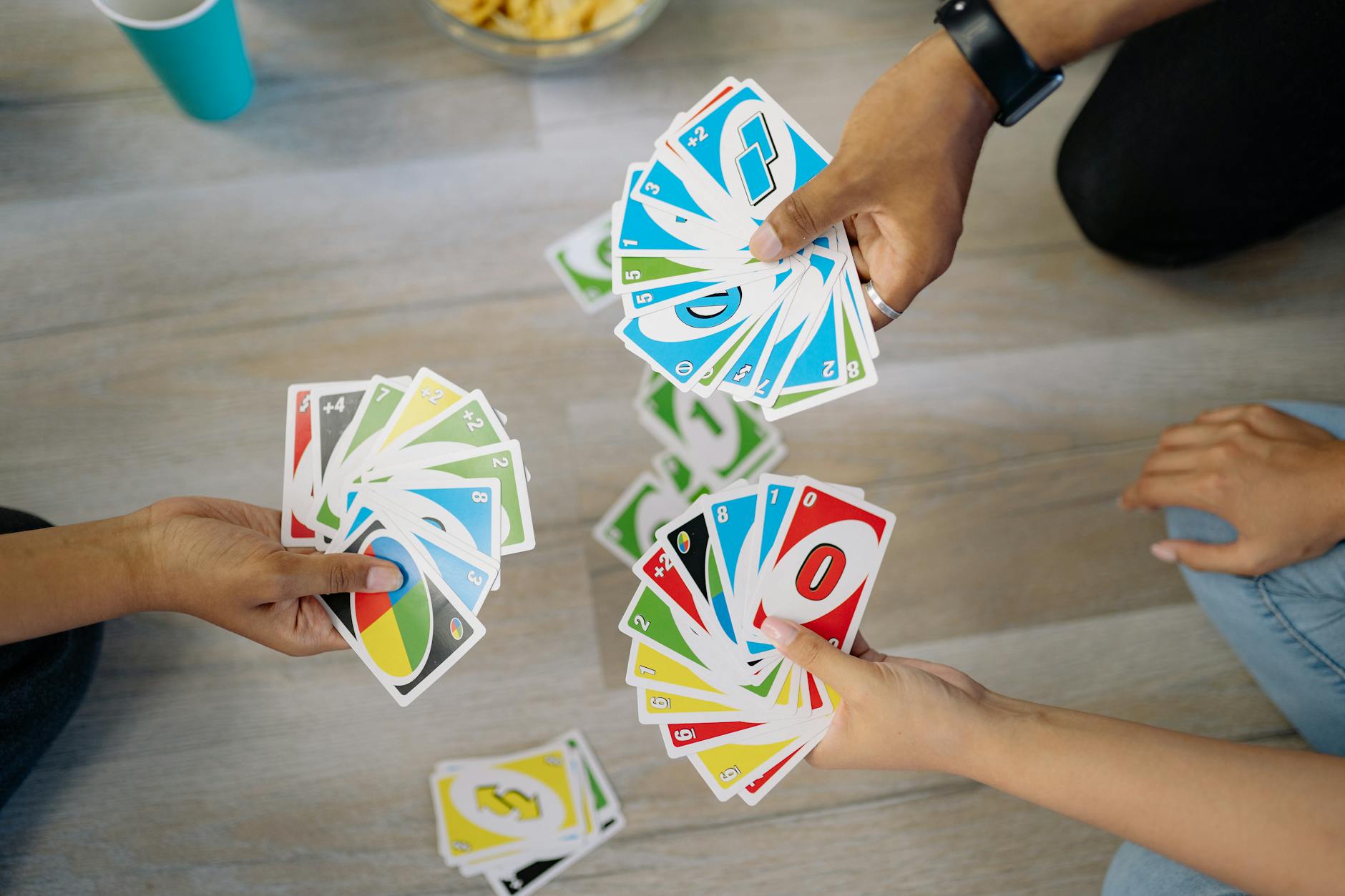 three hands with fanned out Uno cards