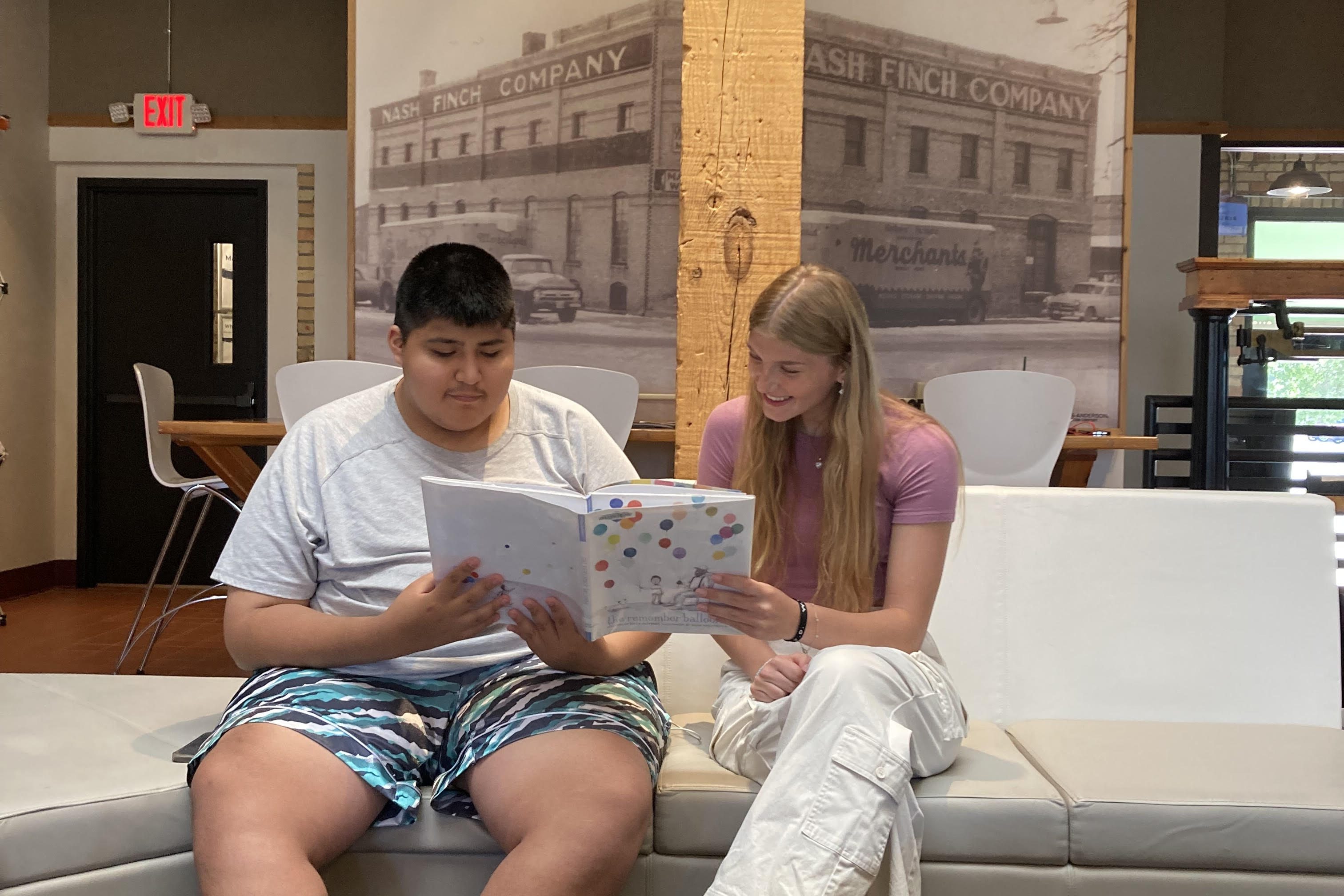 two youth reading a book together on a sofa